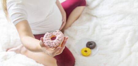 A pregnant woman eats sweet donuts. Selective Focus. Food.の写真素材