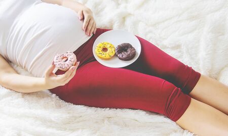 A pregnant woman eats sweet donuts. Selective Focus. Food.の写真素材