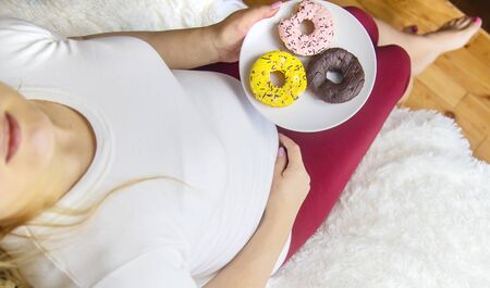 A pregnant woman eats sweet donuts. Selective Focus. Food.の写真素材