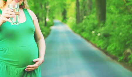 A pregnant woman in a park holds a glass of water. Selective focus. people.の写真素材
