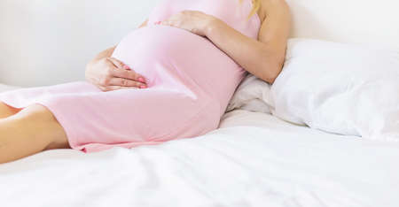 A pregnant woman in bed hugs her stomach. Selective focus. people.の写真素材