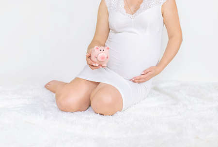 A pregnant woman is holding a piggy bank. Selective focus. people.