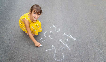 The child writes math on the pavement. Selective focus. summer.