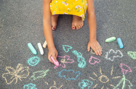 The child draws on the asphalt with chalk. Selective focus. Kid.