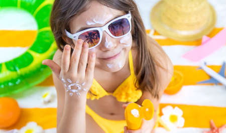 A child girl smears sunscreen on her skin. Selective focus. Kid.