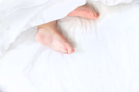 Baby sleeps on a white bed with his feet. Selective focus. Child.の写真素材