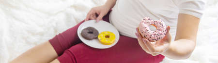 A pregnant woman eats sweet donuts. Selective Focus. Food.の写真素材