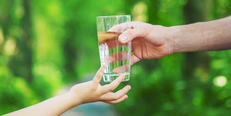 The father gives the child a glass of fresh water. Selective focus. nature.の写真素材