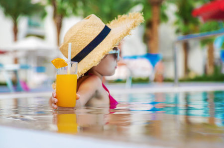 The child is drinking a cocktail by the pool. Selective focus. Kid.