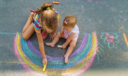 The child draws a house and a rainbow on the asphalt with chalk. Selective focus. Kids.の写真素材