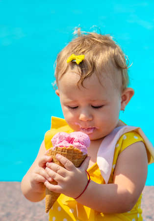 The child is eating ice cream near the pool. Selective focus. Kid.