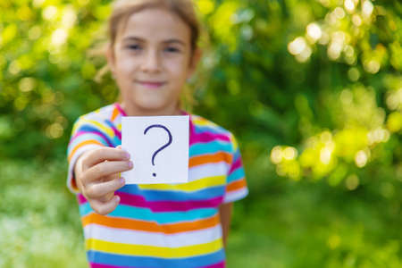 The child holds a paper with a question mark. Selective focus. Kid.