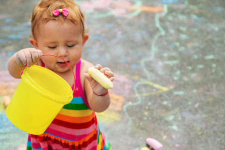 The child draws with chalk on the asphalt. Selective focus. Kid.
