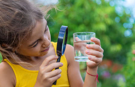 The child examines a glass of water with a magnifying glass. Selective focus. Kid.の写真素材