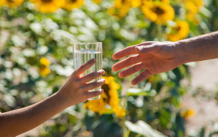 The child and the father are drinking and giving water in a glass. Selective focus. Kid.の写真素材