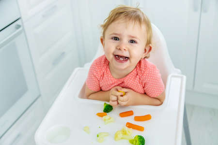 The baby eats vegetables on a chair. Selective focus.の写真素材