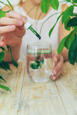 Woman dripping chlorophyll supplement into a glass of water. selective focus. drink.の写真素材