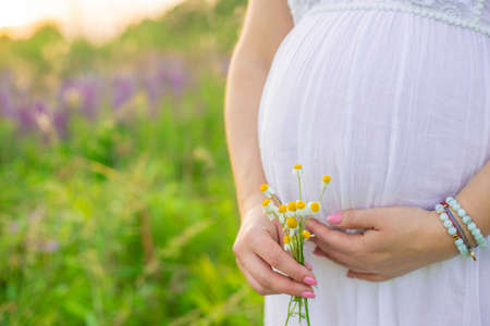 Pregnant woman with a camomile in hands. Selective focus.