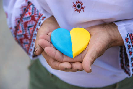 Grandmother holds in her hands a heart in the color of the Ukrainian flag. Selective focus.の写真素材
