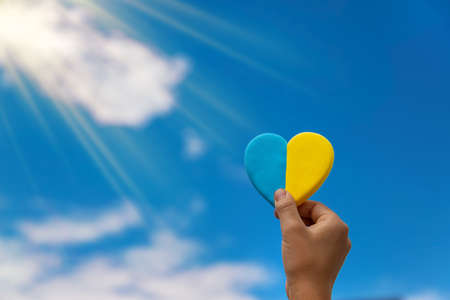 A child holds the heart of Ukraine against the background of the sky. Selective focus.