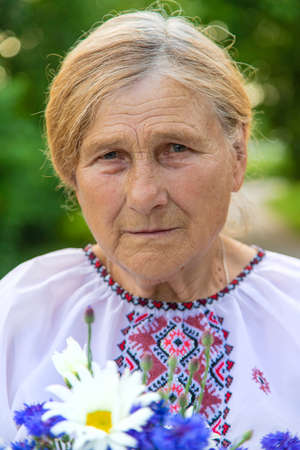 An old Ukrainian woman in an embroidered shirt with a bouquet of flowers. Selective focus.の写真素材