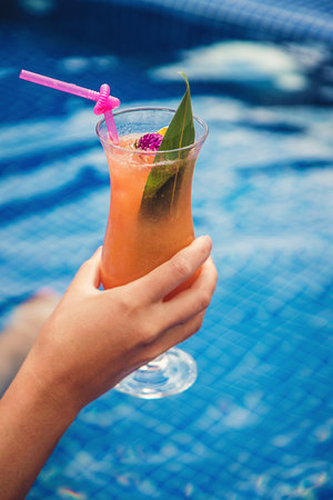 A woman in the pool drinks a cocktail. Selective focus. Kid.