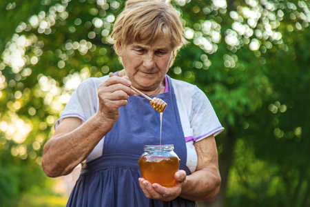 An elderly woman holds honey in her hands, selective focus. People.の写真素材