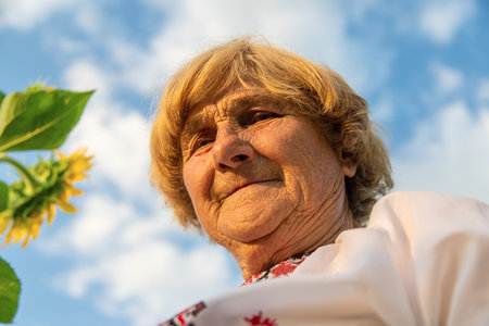 An old woman in a sunflower field wearing an embroidered shirt. Selective focus.の写真素材