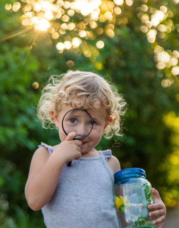 A child looks into a jar with a magnifying glass. Selective focus.の写真素材