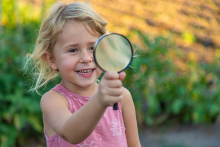 A child looks through a magnifying glass in nature. Selective focus.