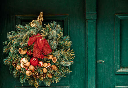 Christmas wreath with fir branches, cones, apples and nuts hangs on a green wooden door. Town house exterior, decorated for Christmas.の写真素材