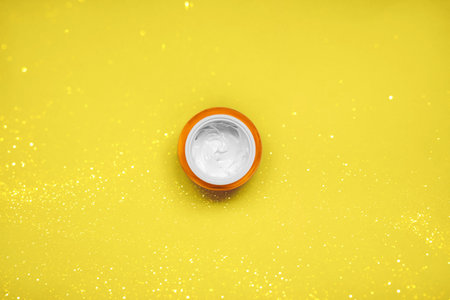 Natural illuminating skin care product with white cream texture on a yellow background with festive...
