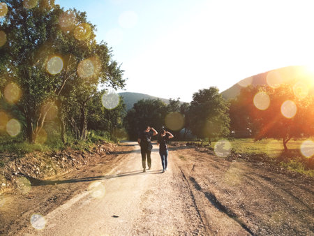 Traveling couple walking along the road in summer. Beautiful sunset lights and bokehの写真素材