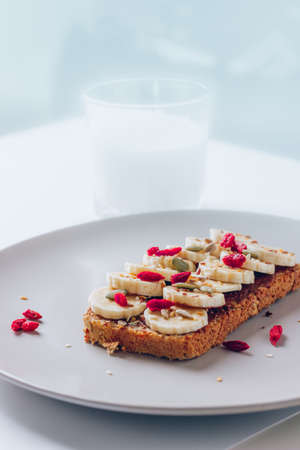 Healthy breakfast toast with chocolate peanut butter, banana, pumpkin, sunflower and flax seeds, sesame, goji berries. Copy spaceの写真素材