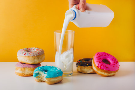 Colorful donuts with chocolate, peanut butter, and jam filling. Man hand pouring plant milk into the glass. Sweet tooth home breakfast for text copyの写真素材