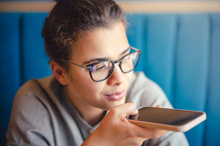 Woman in glasses recording a voice audio message with mobile phone
