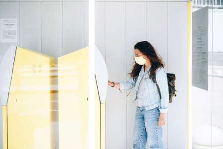 Young woman withdrawing money in face mask at ATM