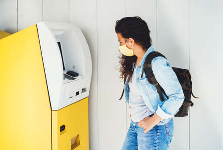 Young woman withdrawing money in face mask at ATMの写真素材