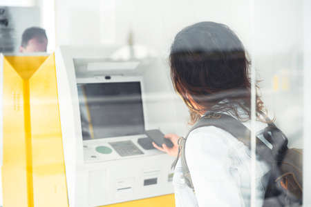 Young woman paying with phone in face mask at ATMの写真素材