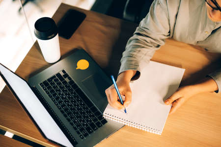 Young woman studying online courses with a laptop, notebook and coffee