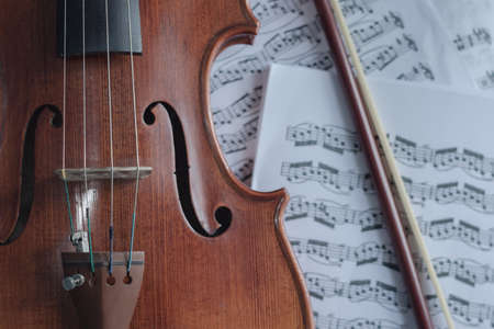 Close up detail on violin body, bow and music notes background. Classic instrument with copy space areaの写真素材