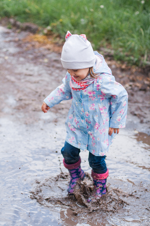 Little girl jumping in muddy puddle and smilingの写真素材