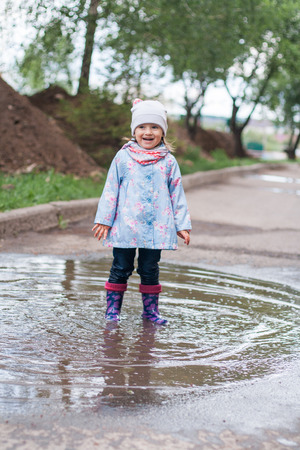 Little girl jumping in muddy puddle and smilingの写真素材
