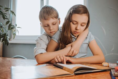 The boy and girl reading book at home during CoVid-19 quarantine, distance learning online with a laptop, a child doing homework for school. Children stayed at home.の写真素材
