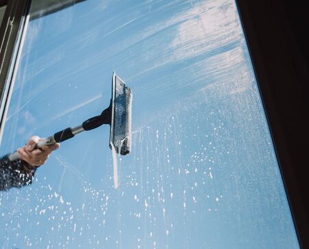 Window cleaner using a squeegee to wash a windowの写真素材