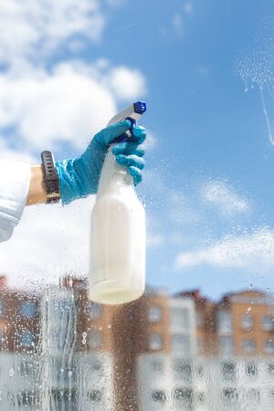 Woman cleaning a window using clean sprayer in action with blue gloves. The concept of cleanlinessの写真素材