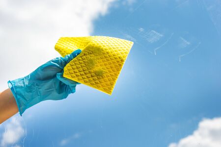 Human hand holding napkin for cleaning window on grey background. A female hands in bright blue gloves washes the windows. The concept of cleanlinessの写真素材