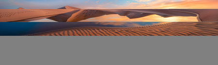 Desert Oasis at Sunrise with Calm Reflective Water and Golden Sand Dunes. Concept of Tranquility, Natural Beauty, and Peaceful Landscapes. Banner.の写真素材