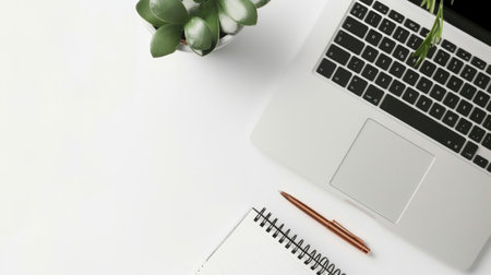 Top view of a silver laptop with a plant and a notepad on a white desk. Concept of office workspace, minimalist design, productivity, modern technology. Copy space.の写真素材