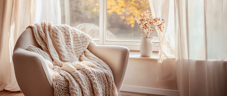 Cozy chair by the window with sunlight and warm blanket. concept of home comfort, tranquility, relaxing atmosphere.の写真素材